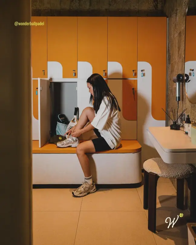 A player lacing up in the orange locker room